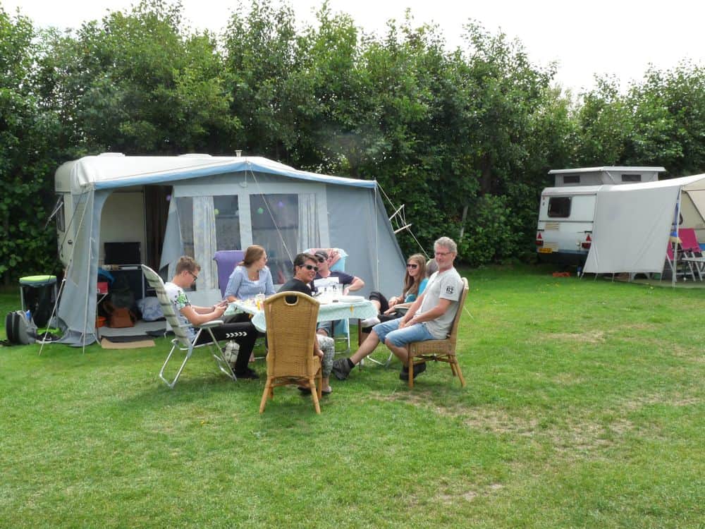 Gasten aan tafel voor hun caravan met voortent