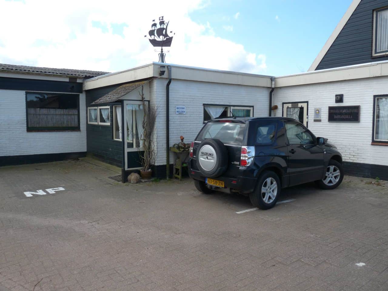 Het gebouw met de vakantiewoning en de parkeerplaats van de minicamping