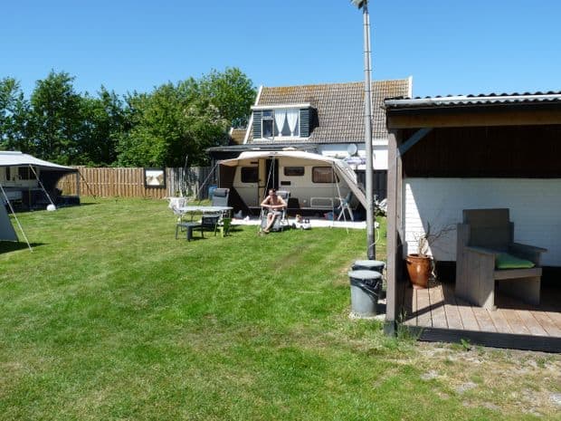 Het grasveld met een caravan en het woonhuis op de achtergrond
